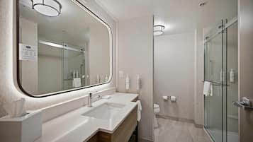 A modern bathroom with a large mirror, dual sinks, a glass shower enclosure, and a toilet.
