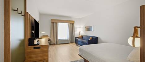 Ein Hotelzimmer mit einem Bett, einem Schreibtisch, einem Stuhl, einem Fernseher, einer Lampe und einem fenster mit Vorhängen.