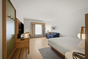 Habitación de hotel con cama, escritorio, silla, televisión, lámpara y ventana con cortinas.