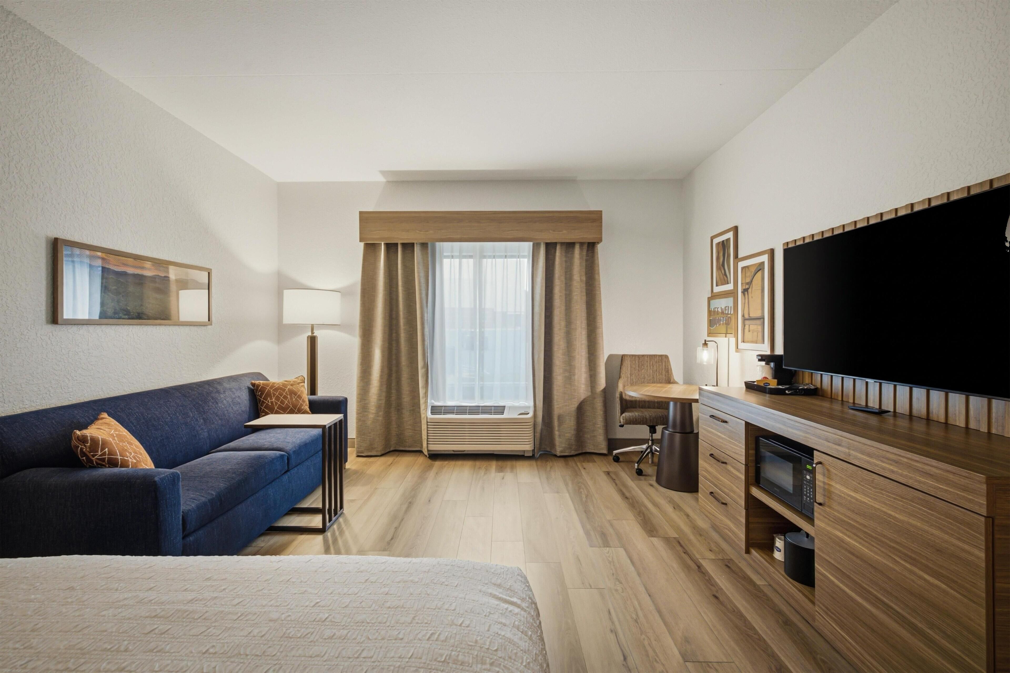 A hotel room with a bed, a sofa, a desk, a television, and a window with curtains.