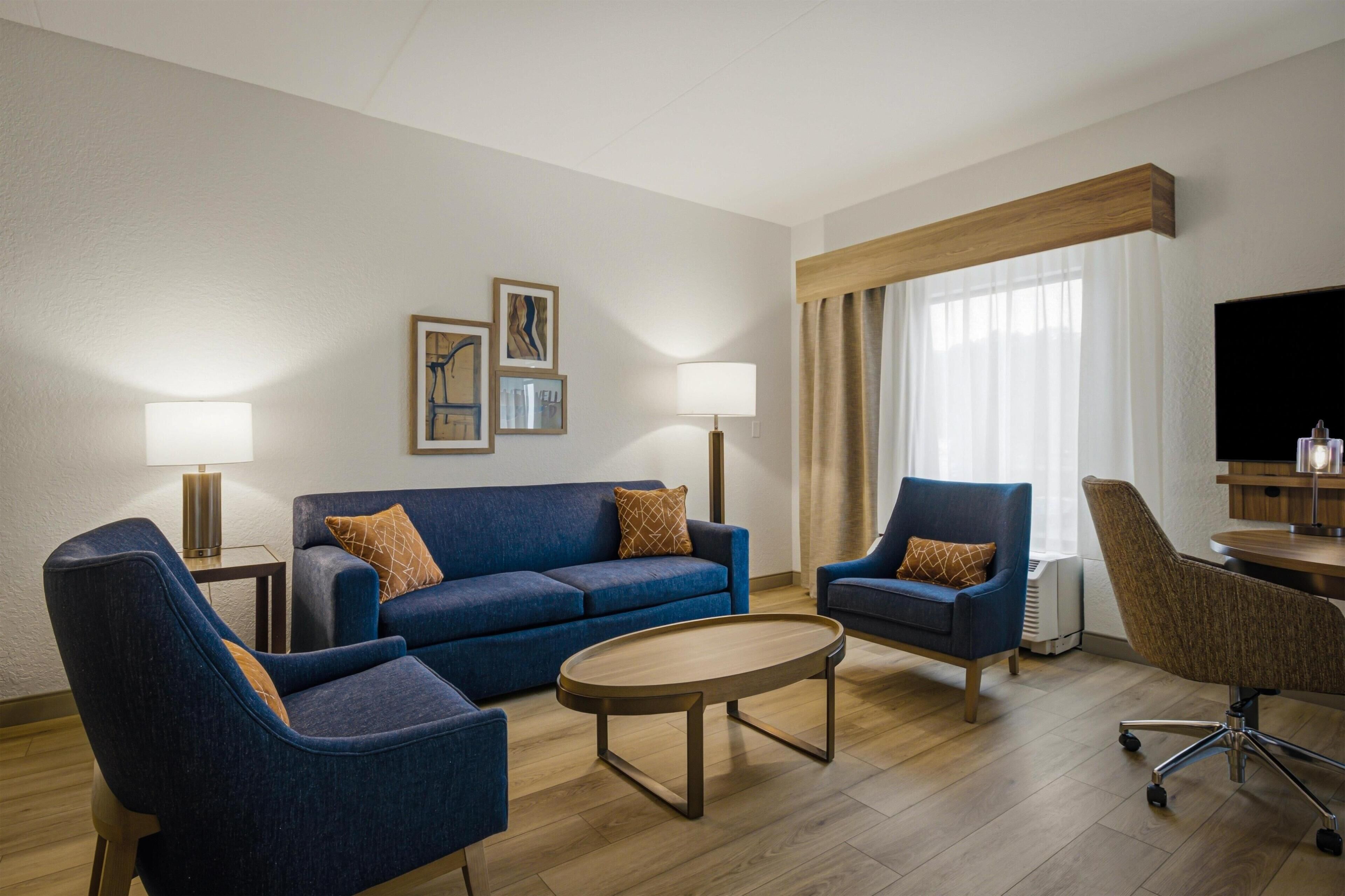 Una habitación de hotel moderna con un sofá azul, dos sillones, una mesita de centro y un televisor.