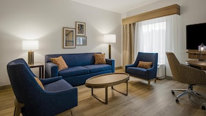 A modern hotel room with a blue sofa, two armchairs, a coffee table, and a TV.