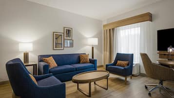 Una habitación de hotel moderna con un sofá azul, dos sillones, una mesita de centro y un televisor.