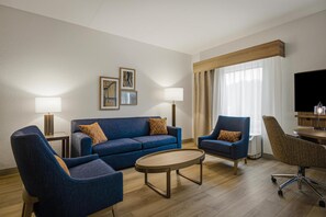 A modern hotel room with a blue sofa, two armchairs, a coffee table, and a TV. - Hampton Inn Hickory (Hickory)