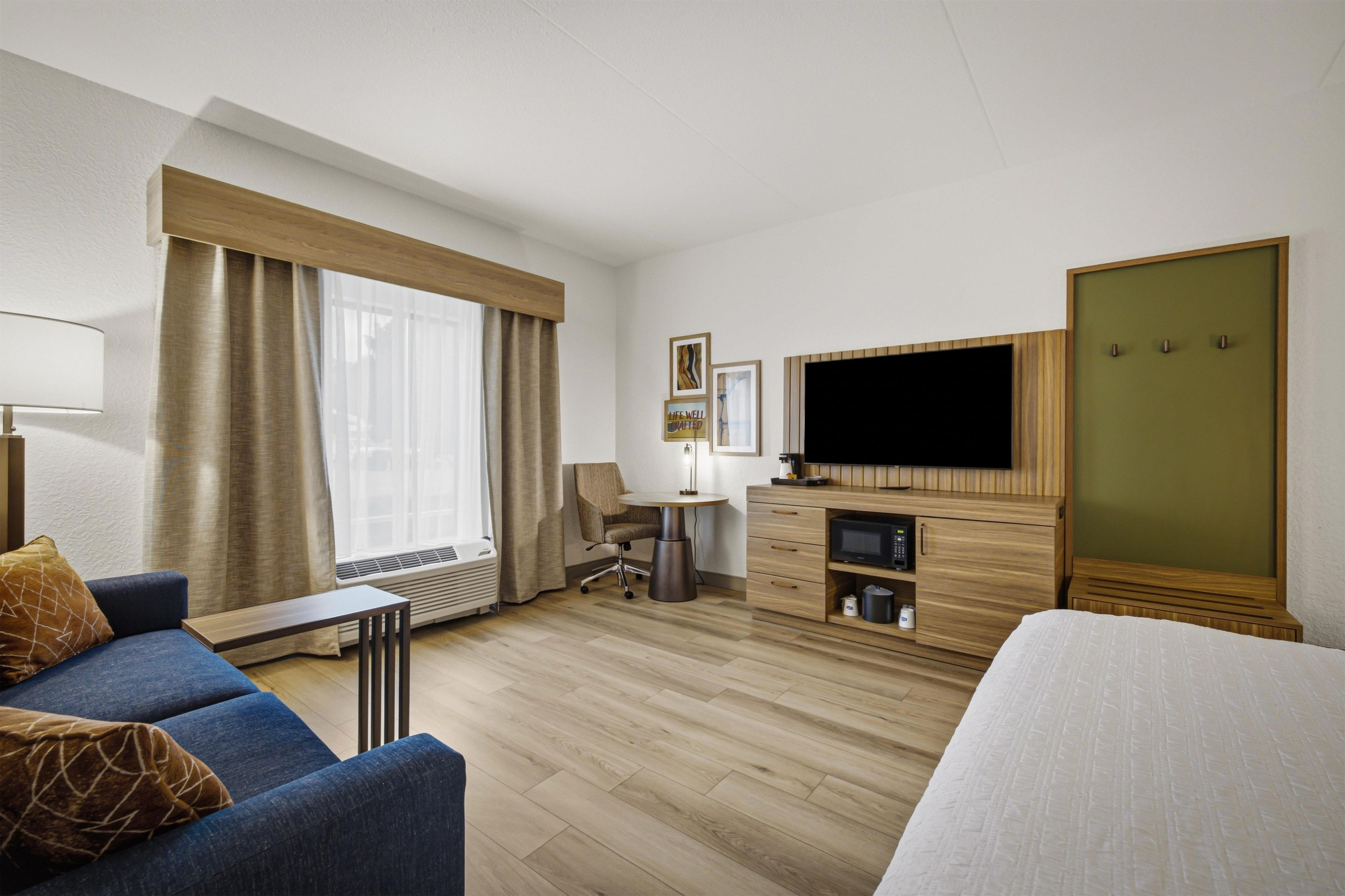 A hotel room with a bed, a sofa, a desk, a television, and a wardrobe.