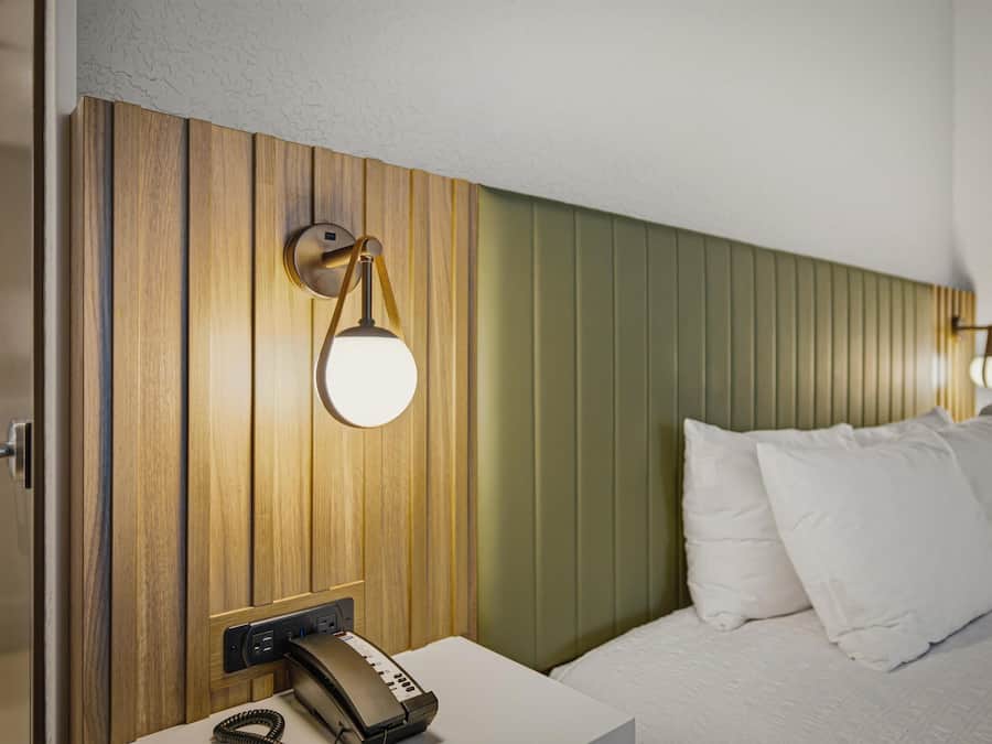 Habitación de hotel con cabecera de madera, mesita de noche con teléfono y dos lámparas de pared.