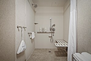 A modern shower area with a handheld showerhead, a towel rack with a white towel, and a shelf with toiletries.