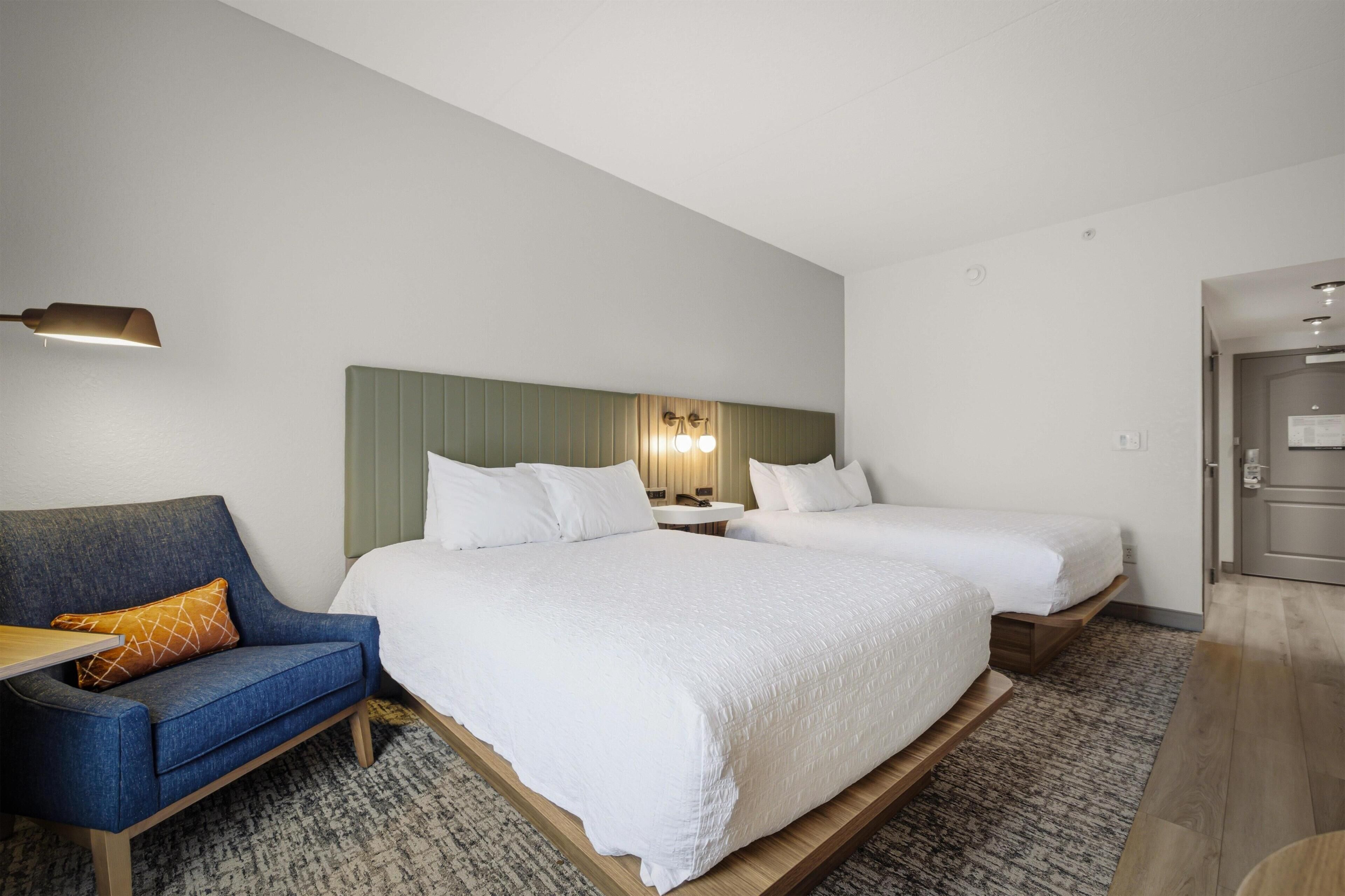 Habitación de hotel con dos camas, un sofá, una mesita y un espejo.