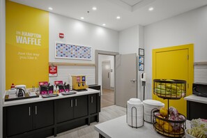 Un área de cocina moderna con pared amarilla, una estación de café y una exhibición de frutas.