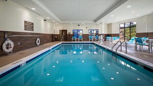 A swimming pool with a lifeguard stand, a sign warning of no lifeguard on duty, and a view of the outside through large windows.