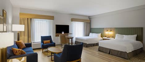 A hotel room with a bed, two sofas, a TV, and a desk.