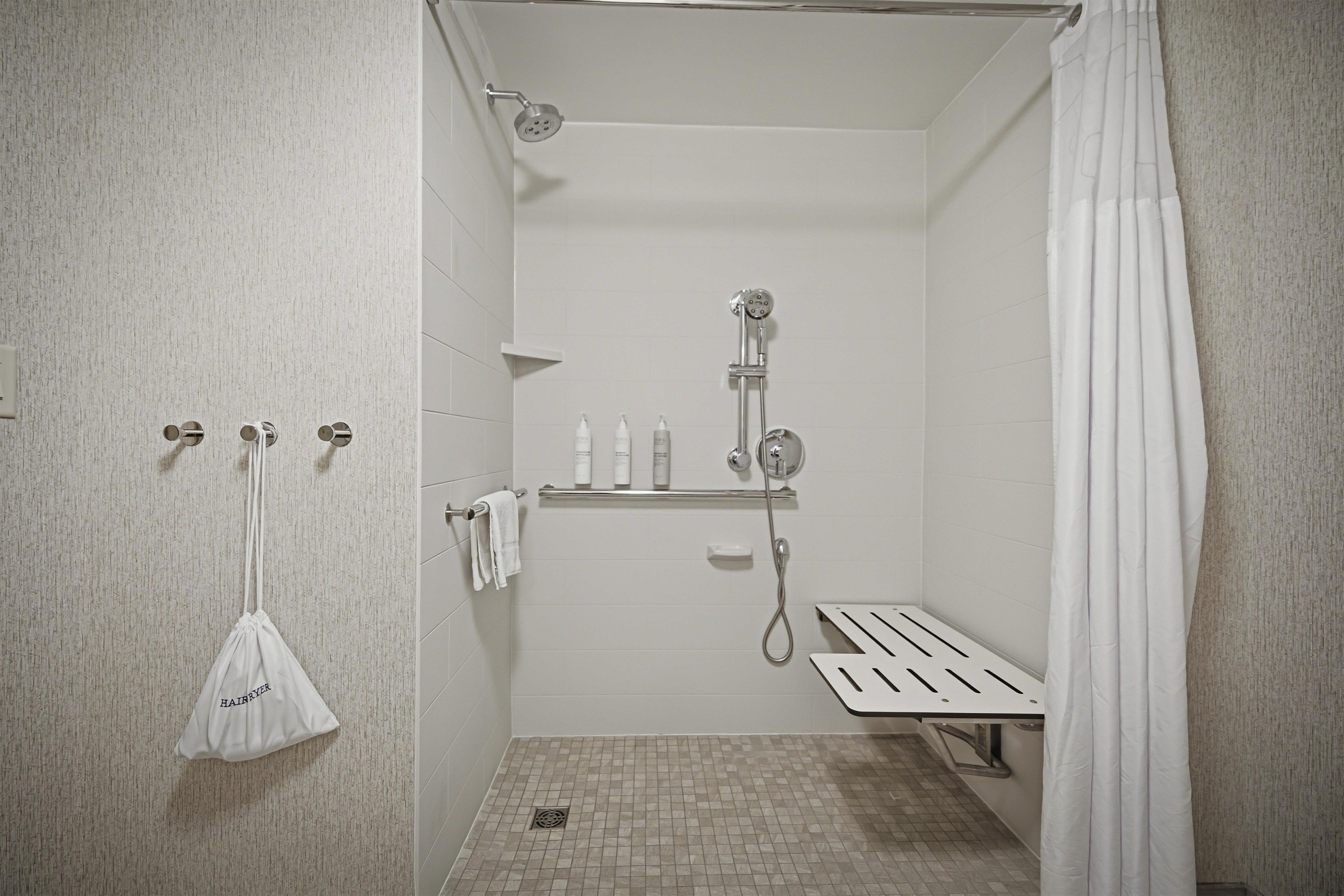 Un baño pequeño y moderno con ducha, un perchero y una repisa con artículos de aseo.