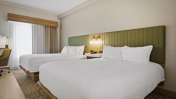 Une chambre d’hôtel avec deux lits, un bureau, une chaise et une fenêtre avec des rideaux.