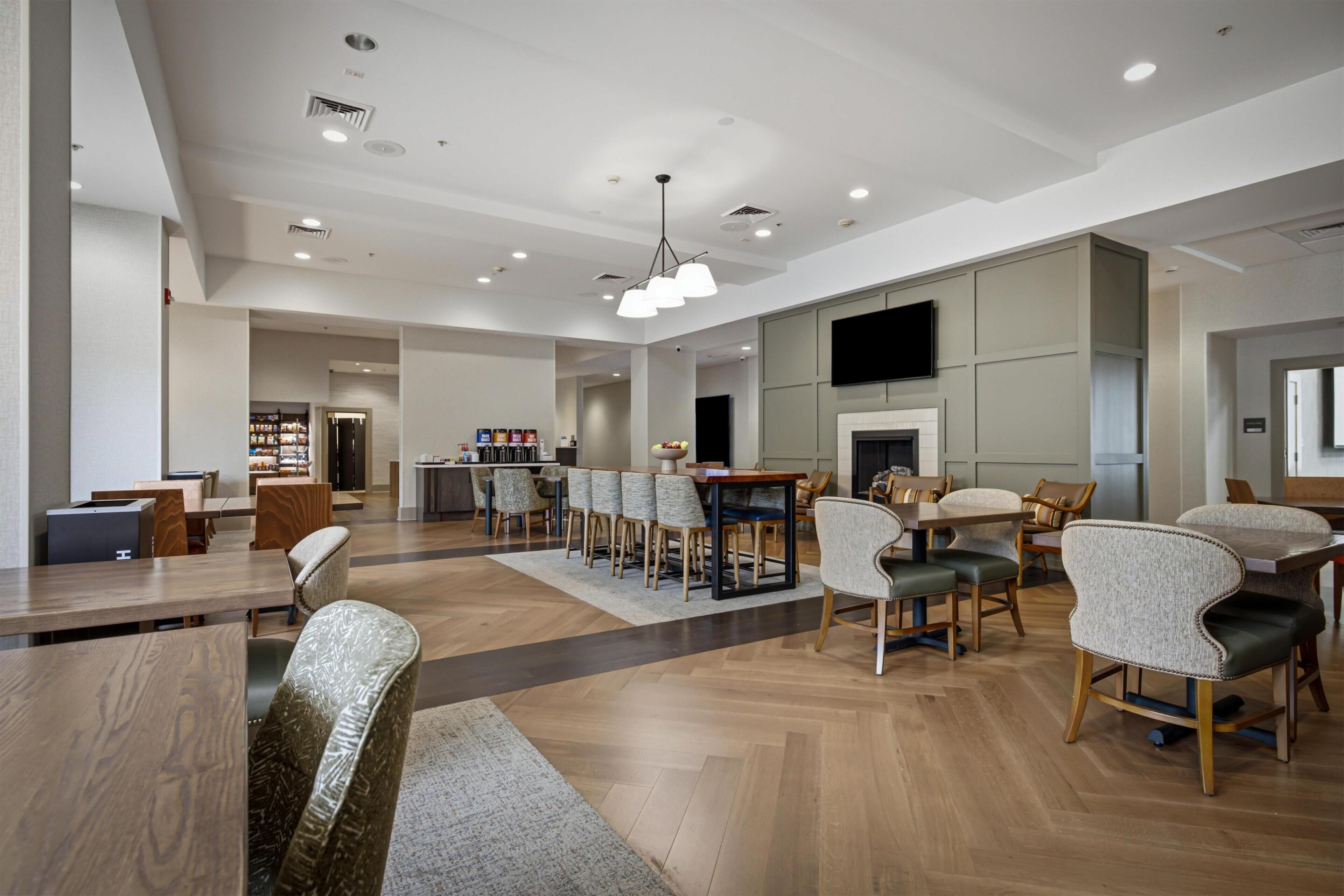 A spacious hotel lobby with multiple seating areas, a bar, and a television mounted on the wall.
