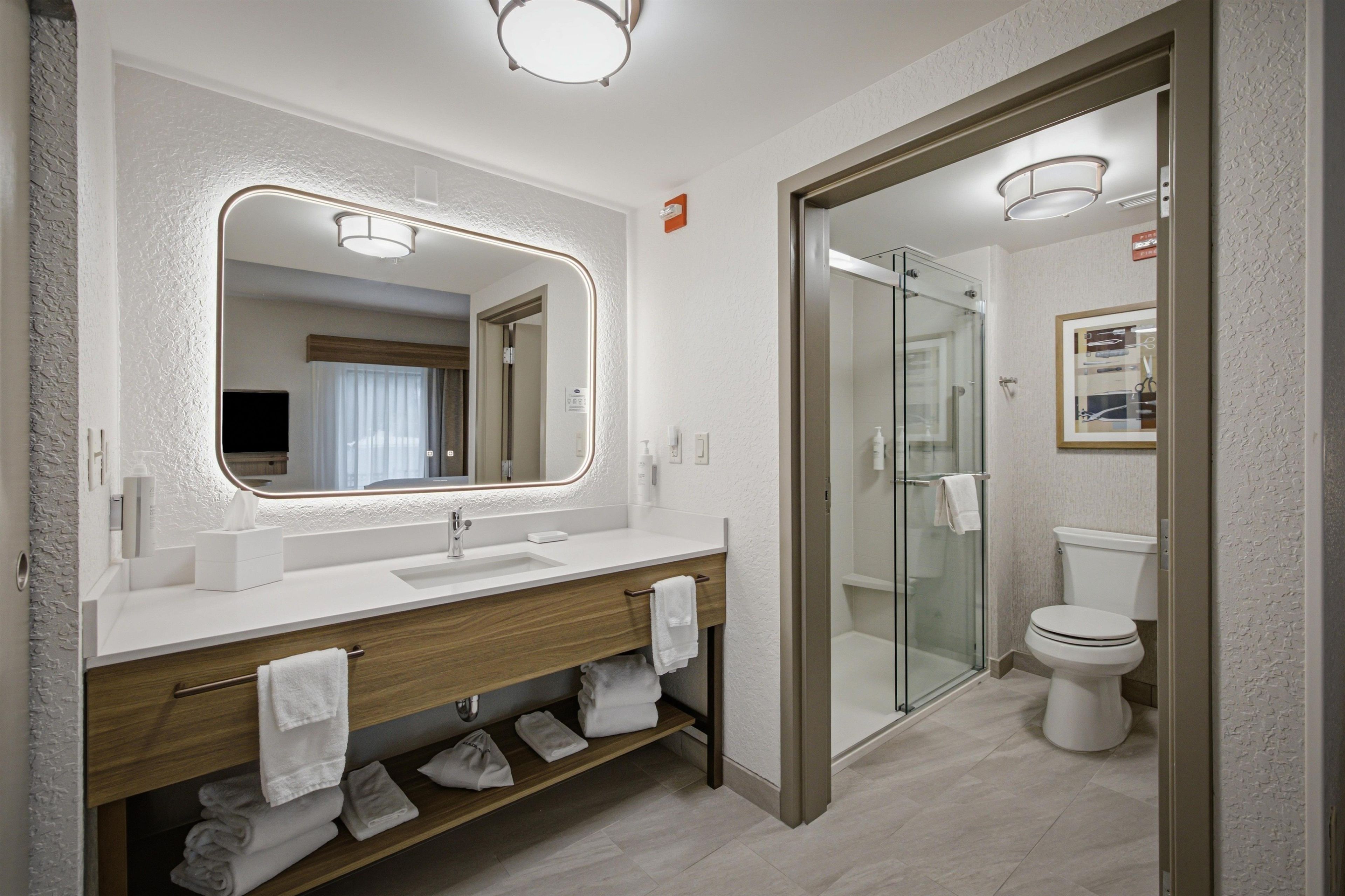 A modern bathroom with a large mirror, a sink, a shower, and a toilet.
