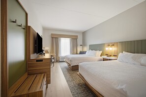 Quarto de hotel com duas camas, uma escrivaninha, televisão e uma janela com cortinas.