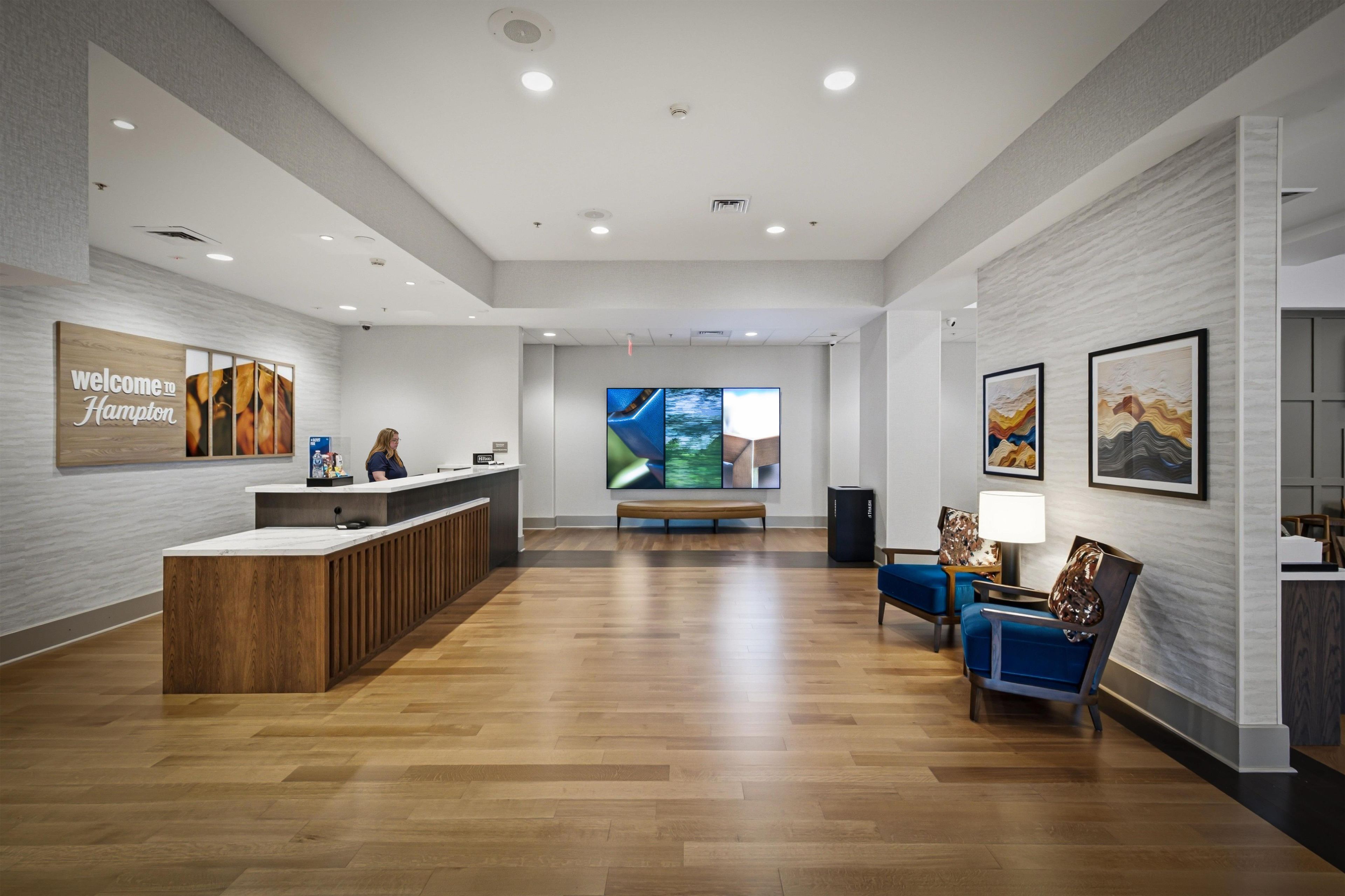 A hotel reception area with a wooden reception desk, a bench, and a seating area with chairs.