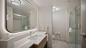 A modern bathroom with a large mirror, dual sinks, a glass shower enclosure, and a toilet.