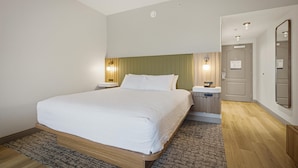 A hotel room with a large bed, bedside tables, a mirror, and a door leading to a bathroom.
