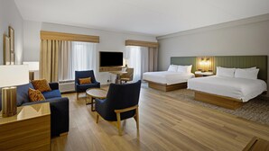 A hotel room with two beds, a sofa, a chair, a TV, and a desk.