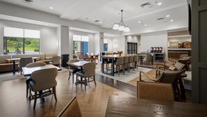 A spacious hotel lobby with multiple seating areas, a central bar, and large windows offering a view of the outdoors.