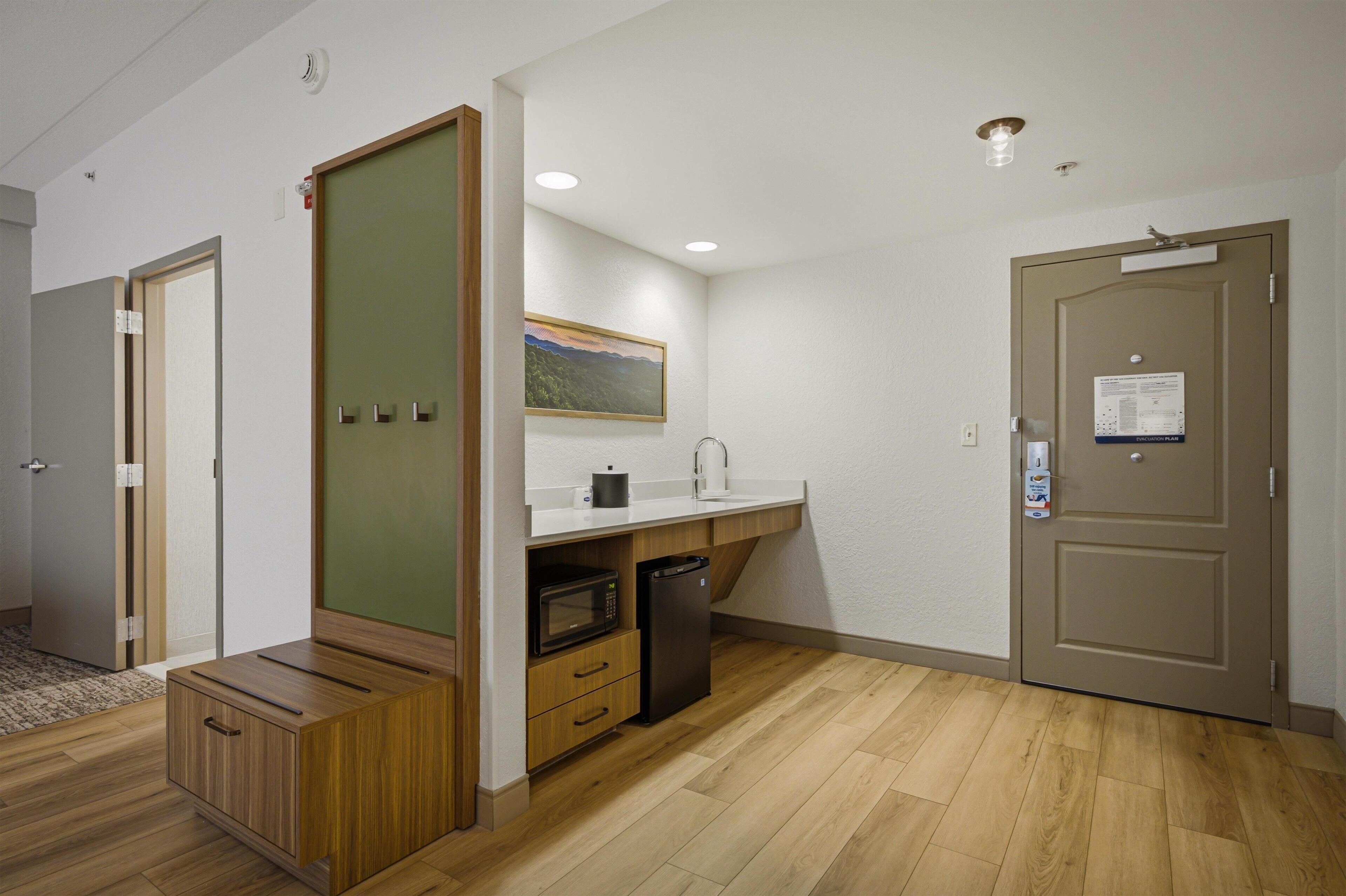 Una kitchenette compacta con microondas, cafetera y refrigerador pequeño.