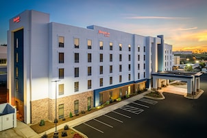 Un moderno hotel Hampton Inn con fachada plana, varias ventanas y un estacionamiento.