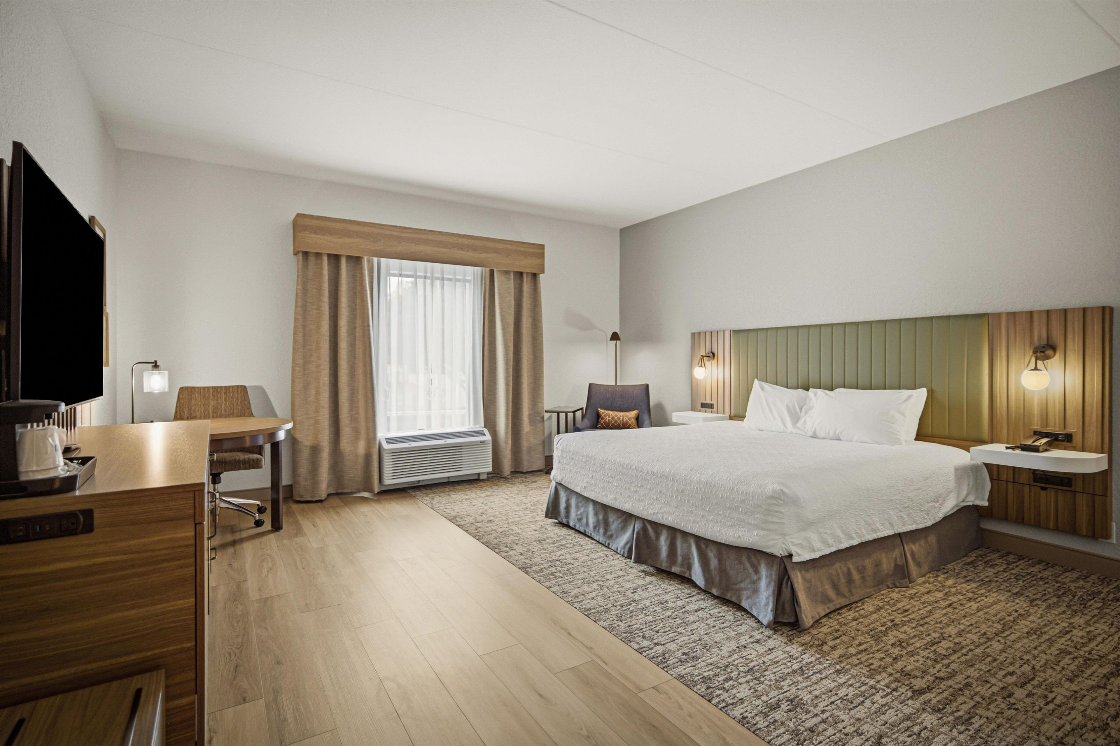 A hotel room with a bed, a desk, a chair, a television, and a window with curtains.