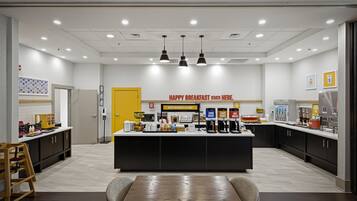 A modern breakfast area with a central counter, seating, and various food and drink dispensers.