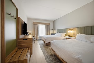 Habitación de hotel con dos camas, un escritorio, un televisor y una ventana con cortinas.