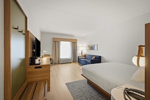 A hotel room with a bed, a desk, a chair, a TV, a lamp, and a window with curtains.