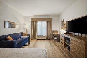 Habitación de hotel con cama, sofá, escritorio, televisor y ventana con cortinas.