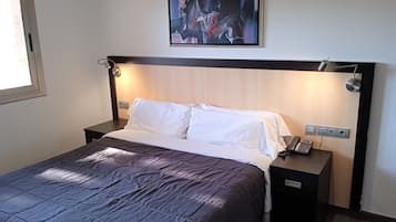 Una habitación de hotel con cama, mesitas de noche, teléfono y un cuadro en la pared.