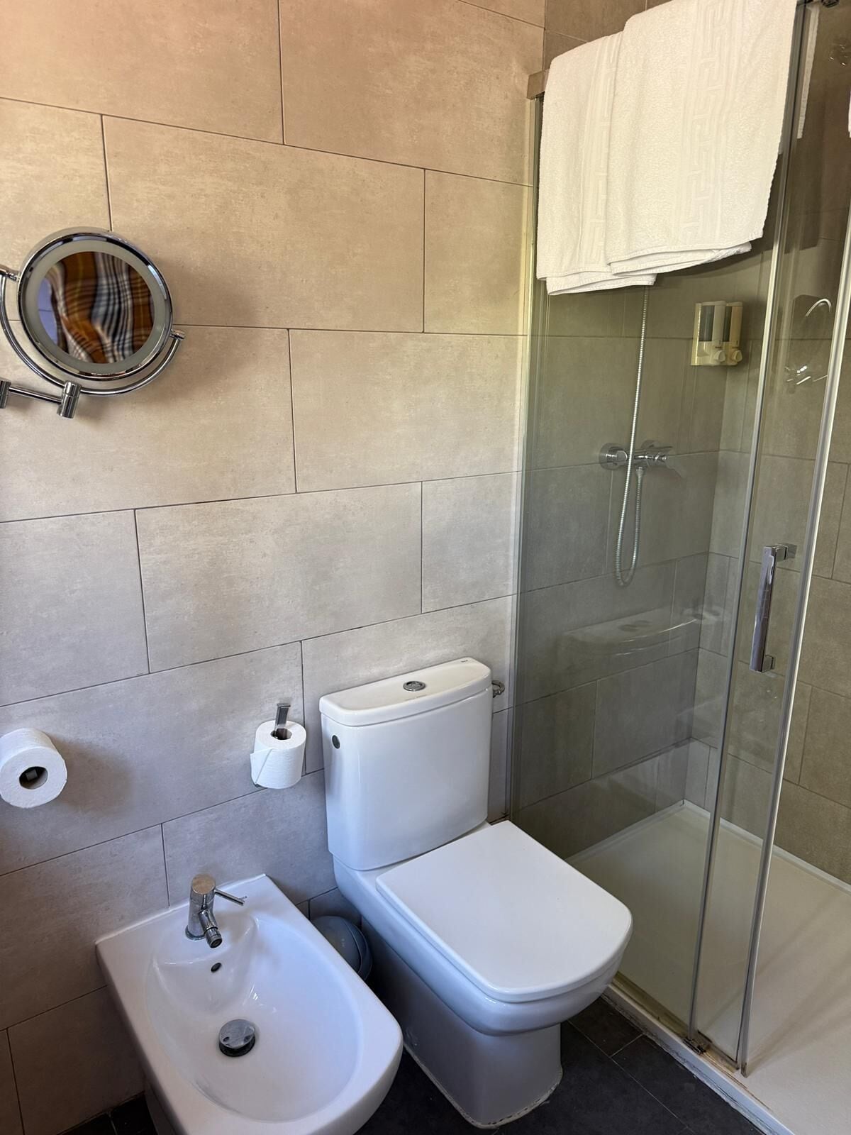 Un baño con inodoro, bidé, lavabo y ducha con mampara de vidrio.