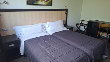 Een hotelkamer met een bed, een bureau, een stoel, een nachtkastje en een schilderij aan de muur.