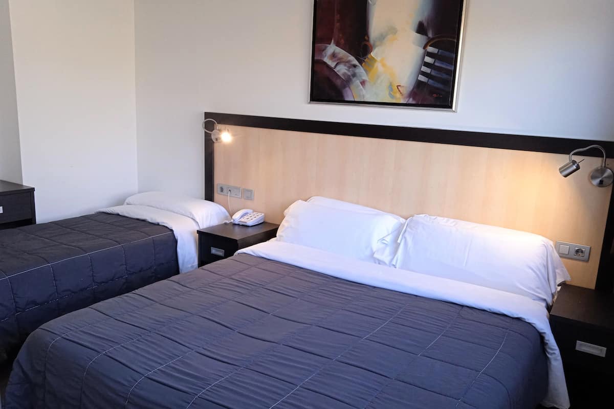 Habitación de hotel con dos camas, un cuadro en la pared, una lámpara de noche y un teléfono en la mesita.