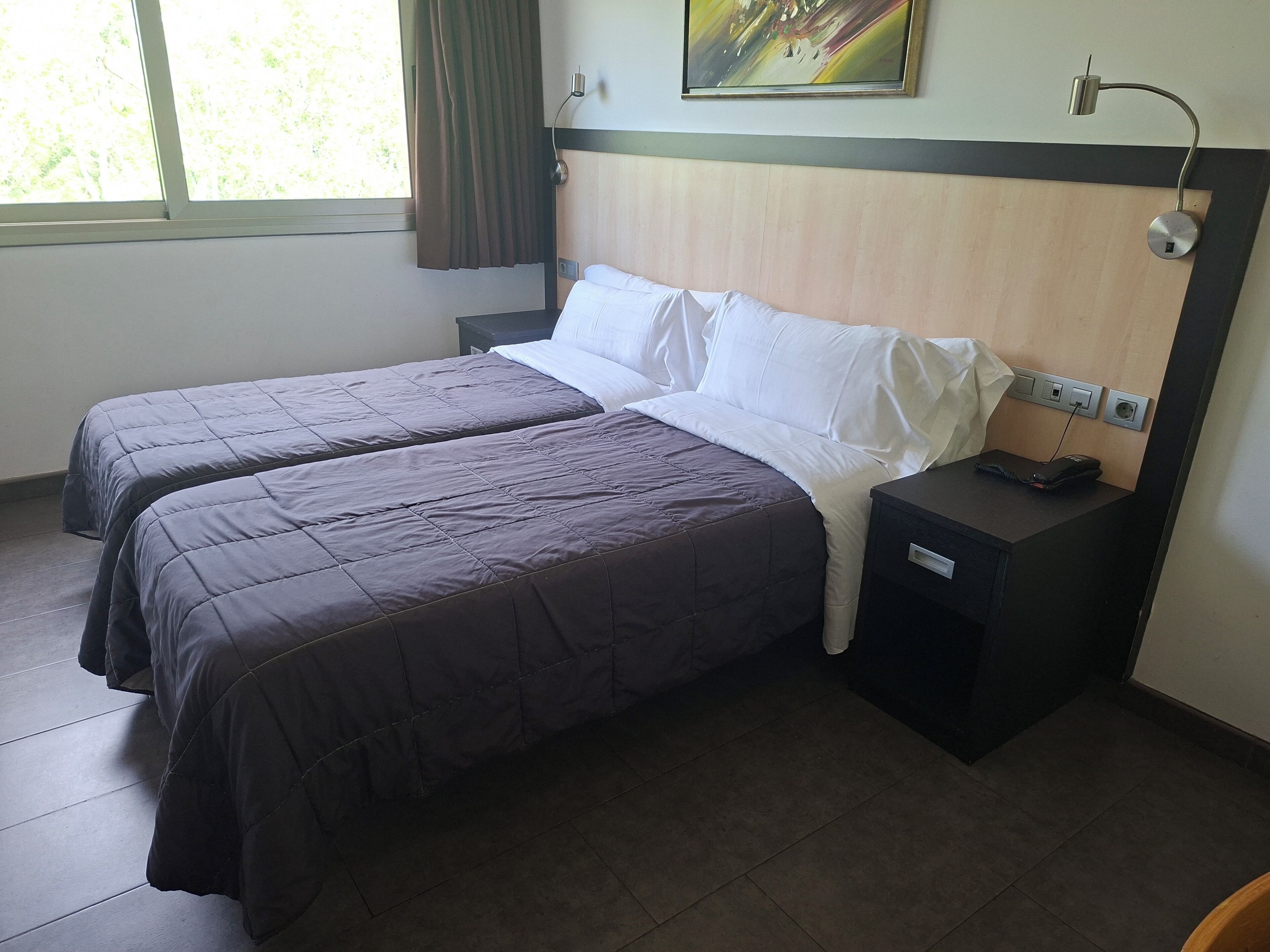 A hotel room with two beds, a nightstand, a lamp, and a painting on the wall.