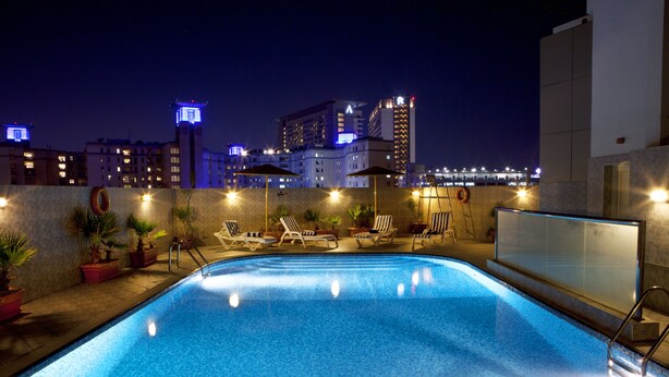 A swimming pool with lounge chairs and umbrellas, surrounded by potted plants. - Landmark Hotel Riqqa (Dubai)