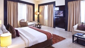 A hotel room with a large bed, a sofa, a TV, and a lamp. - Landmark Hotel Riqqa (Dubai)