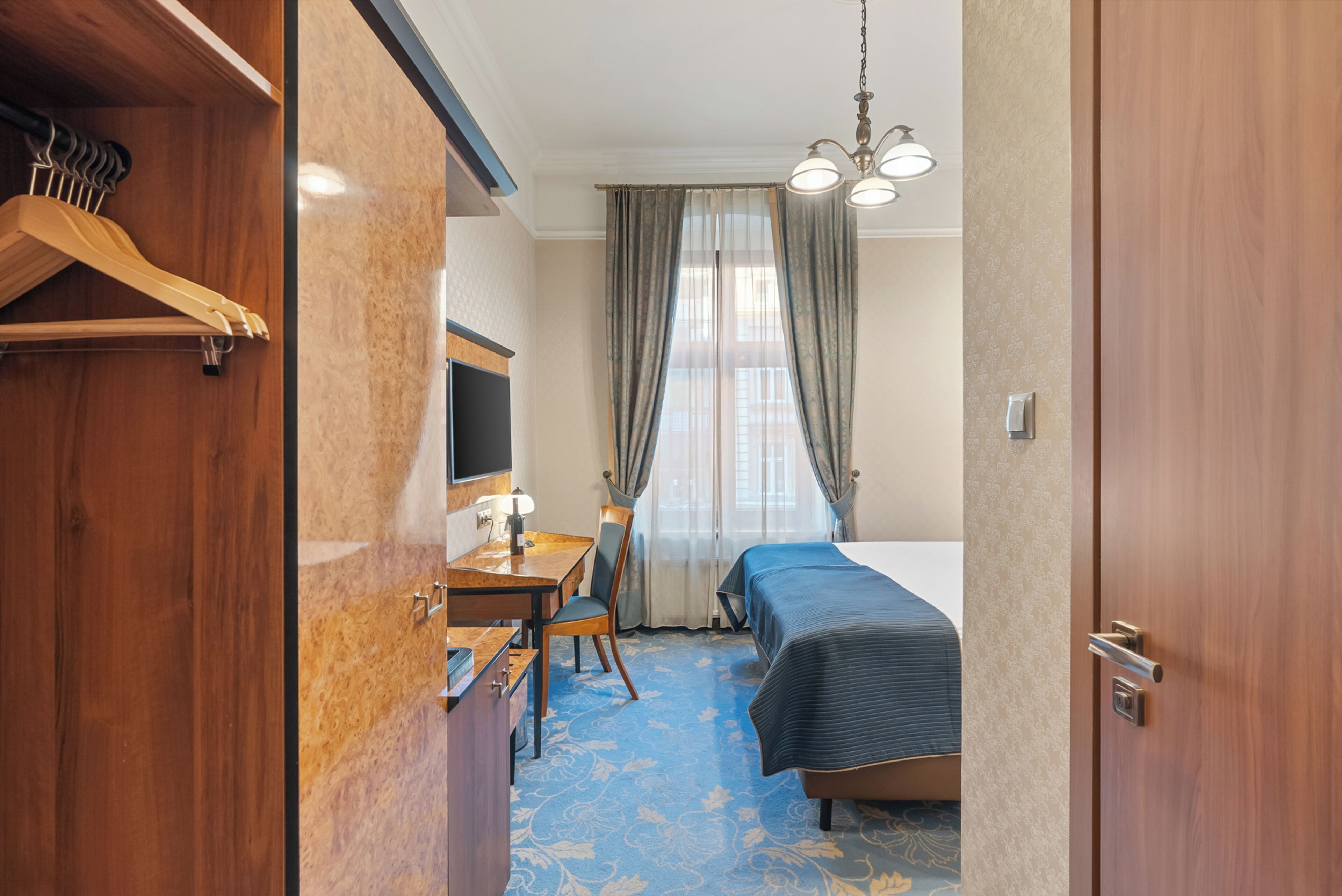 A hotel room with a bed, a desk with a chair, a TV, and a wardrobe.