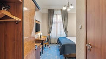A hotel room with a bed, a desk with a chair, a TV, and a wardrobe.