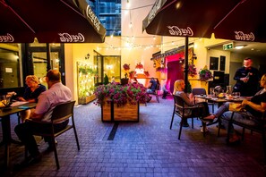 An outdoor dining area with tables and chairs, a wooden planter with flowers, and Coca-Cola branded umbrellas. - Hotel Diament Plaza Gliwice (Gliwice)