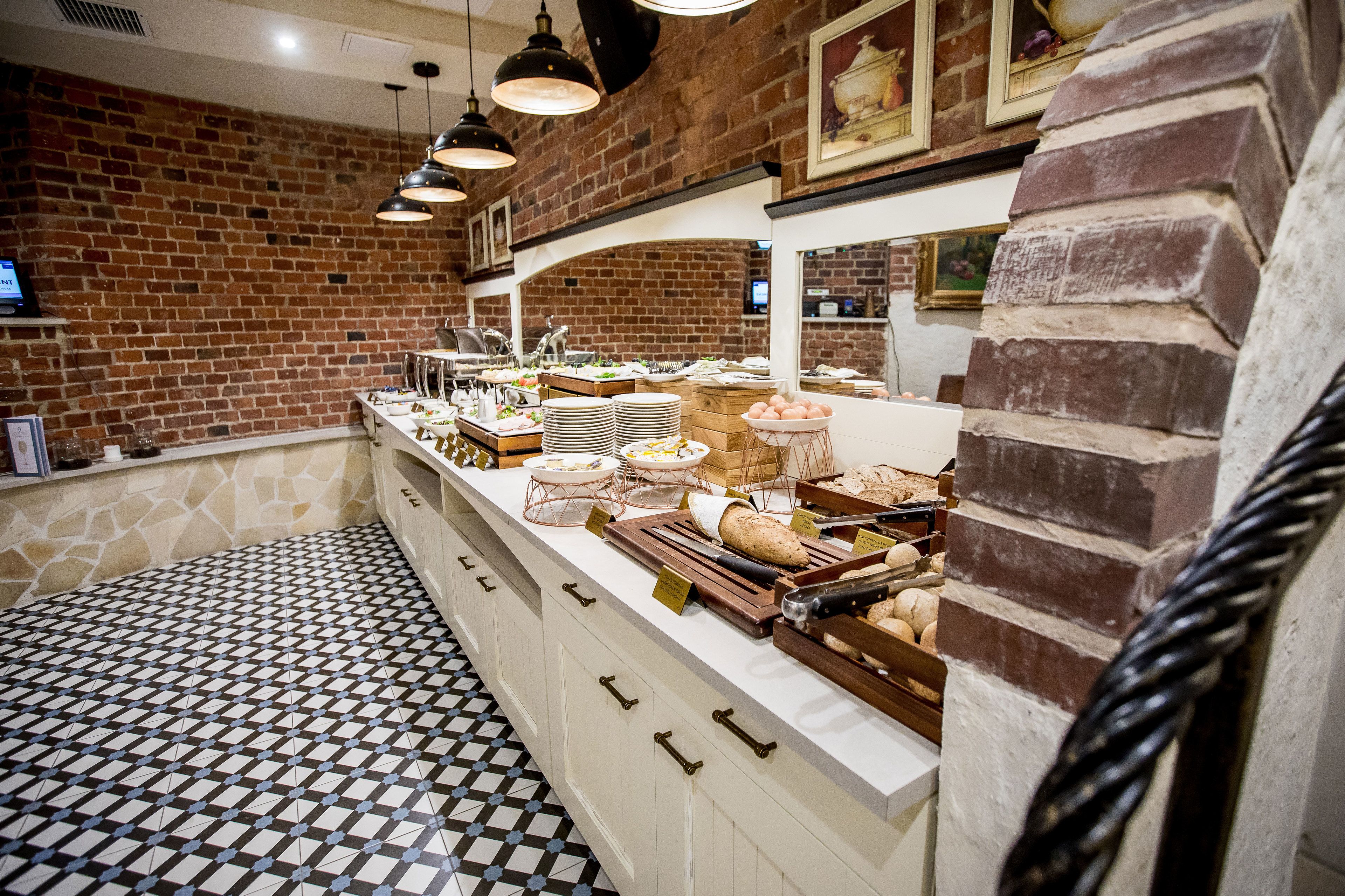 A buffet area with a brick wall, patterned floor, and various food items displayed on a counter.