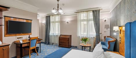 A hotel room with a bed, a desk, a chair, a dresser, and a television.