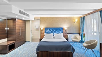 Habitación de hotel con una cama grande, zona de estar con una silla, escritorio y armario.