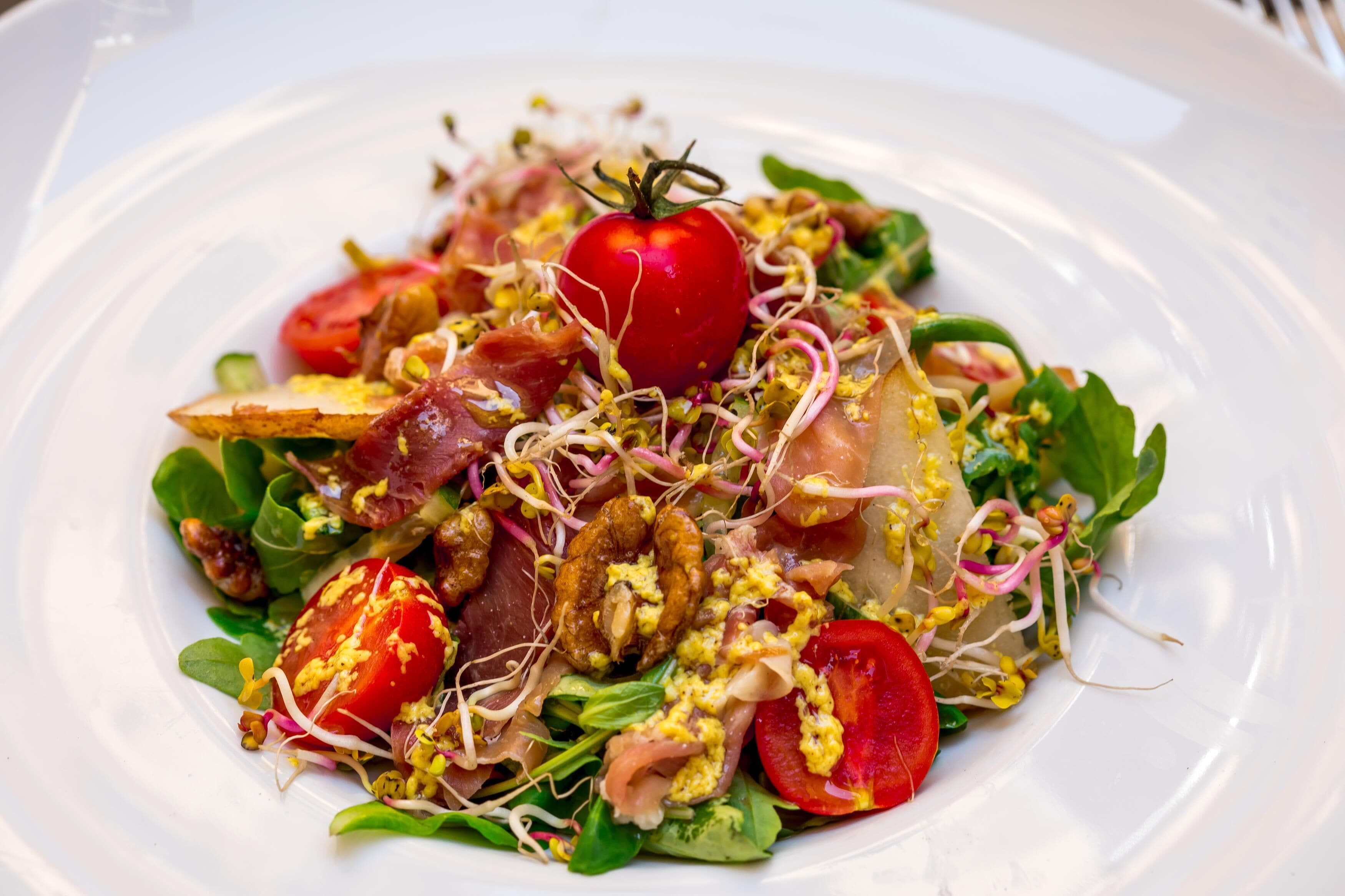 A plate of food with various ingredients like tomatoes, sprouts, and greens.