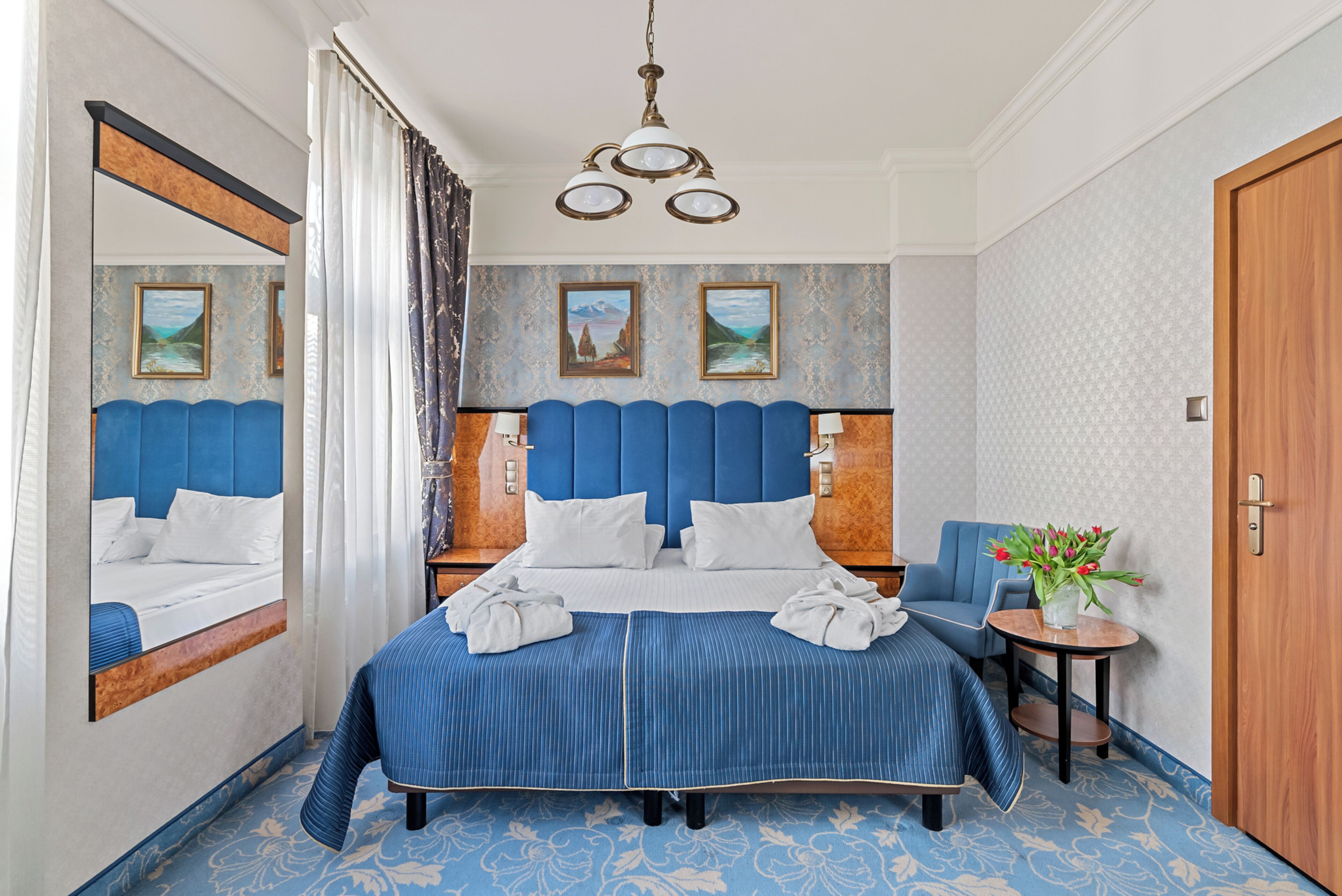 A hotel room with a large bed, a chair, a small table with a vase of flowers, and a door.