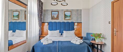 A hotel room with a large bed, a chair, a small table with a vase of flowers, and a door.