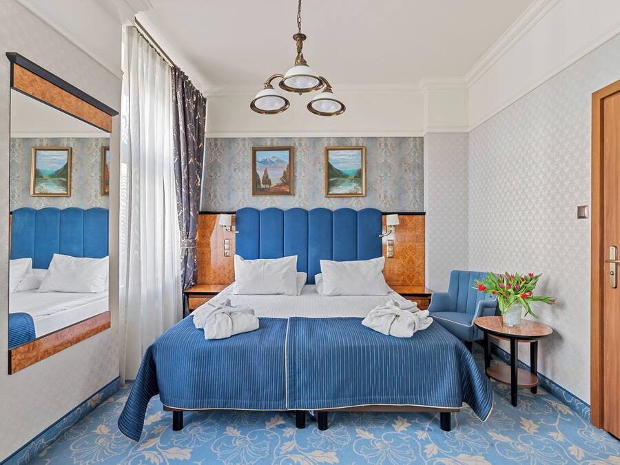 A hotel room with a large bed, a chair, a small table with a vase of flowers, and a door.