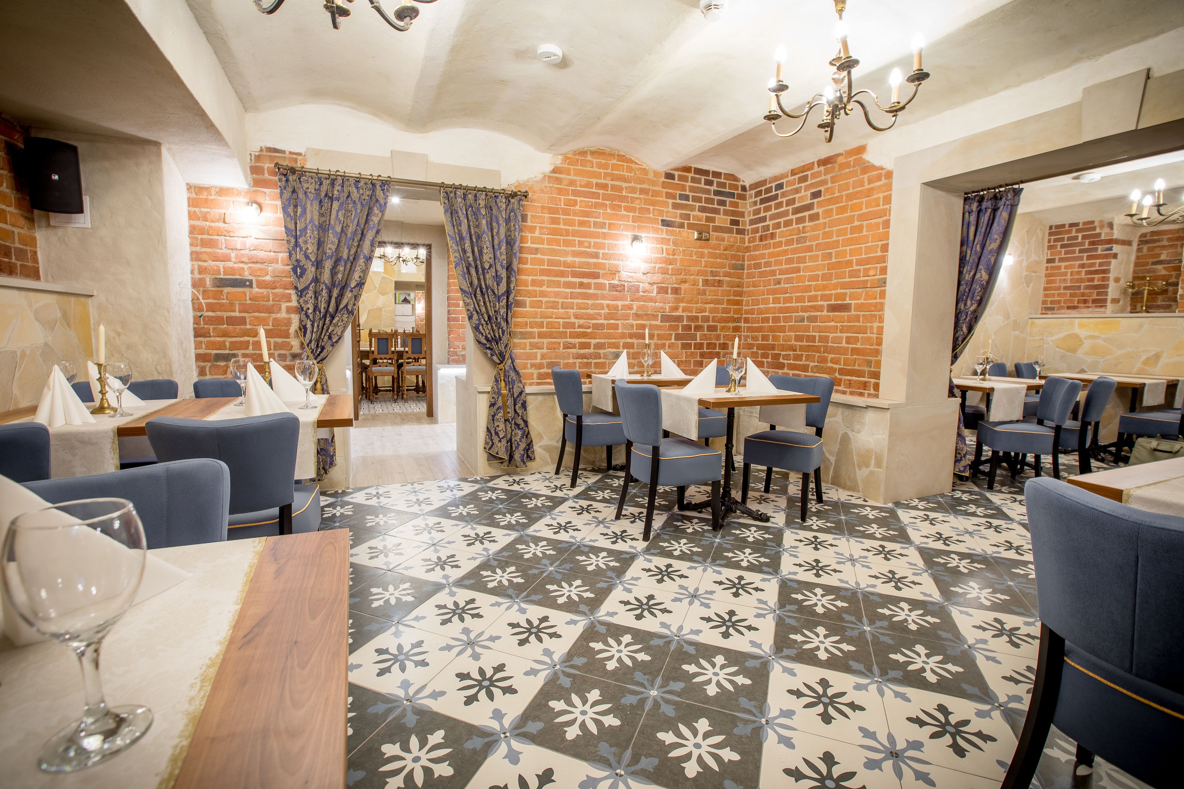 A restaurant with blue chairs, tables with white tablecloths, and a patterned floor.